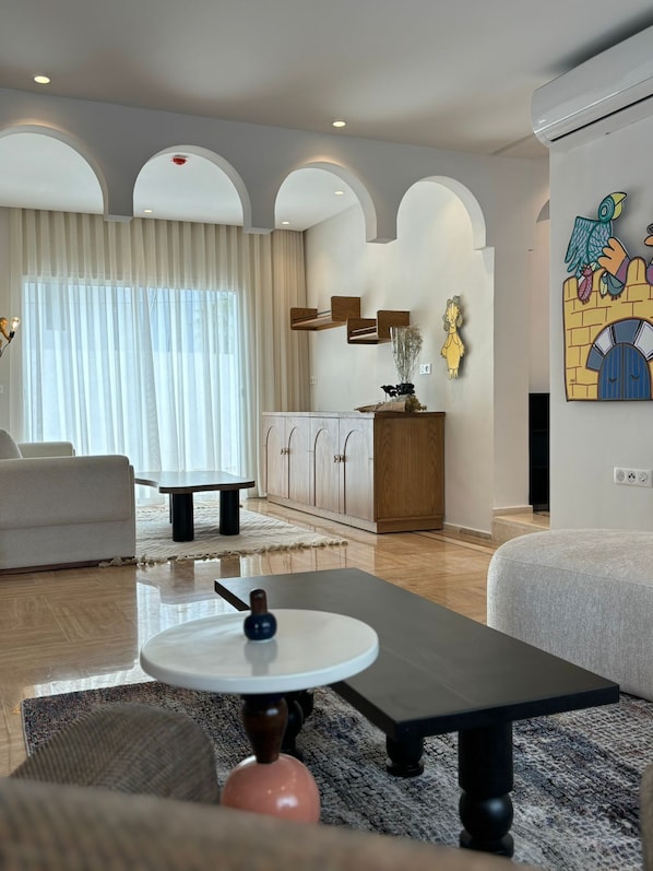 Uma sala de estar moderna com um sofá, uma mesa de centro e uma mesa de jantar. Há um aparador com objetos decorativos e uma obra de arte na parede.