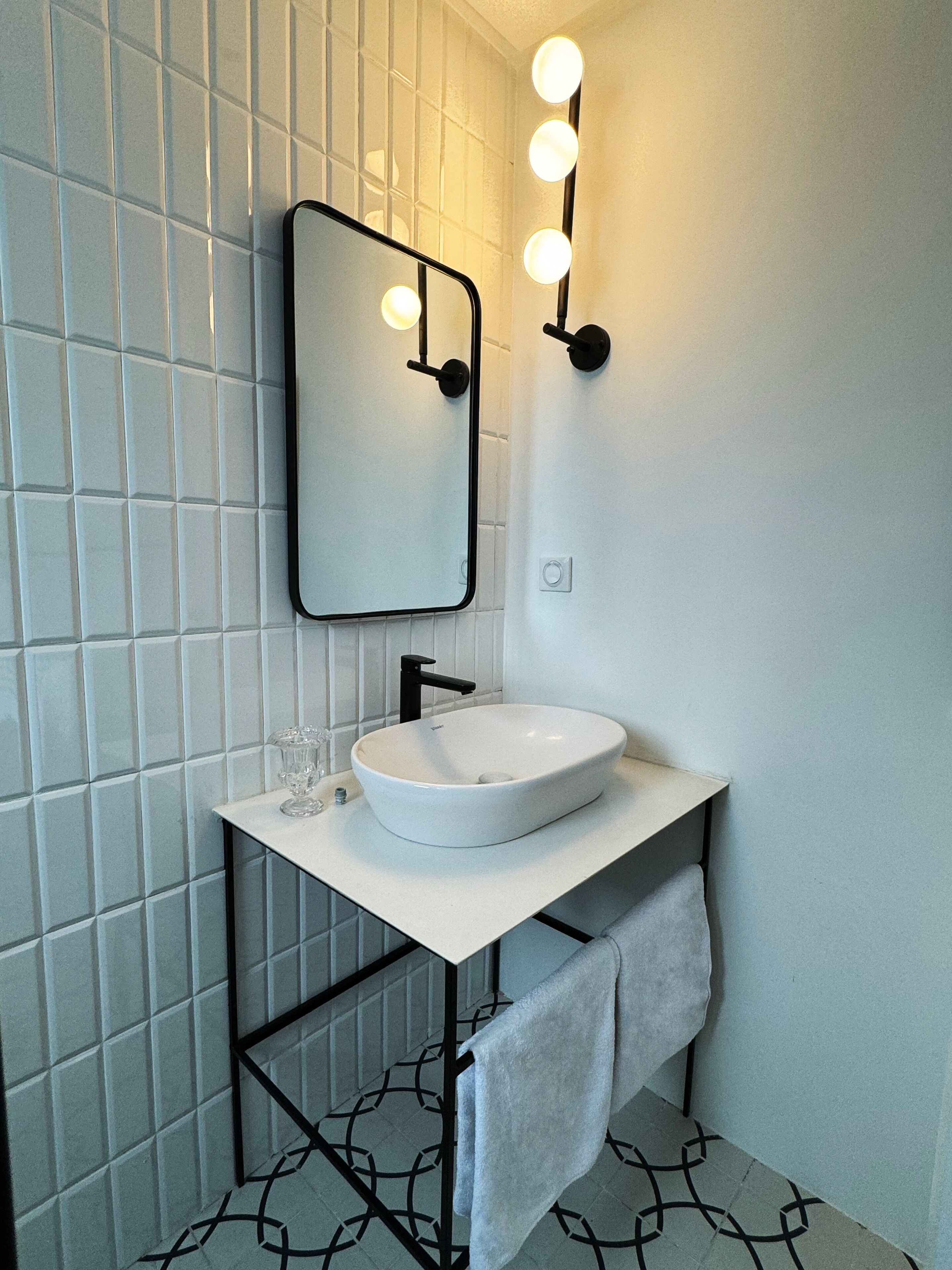 A bathroom with a white sink, black faucet, and a mirror with lights.