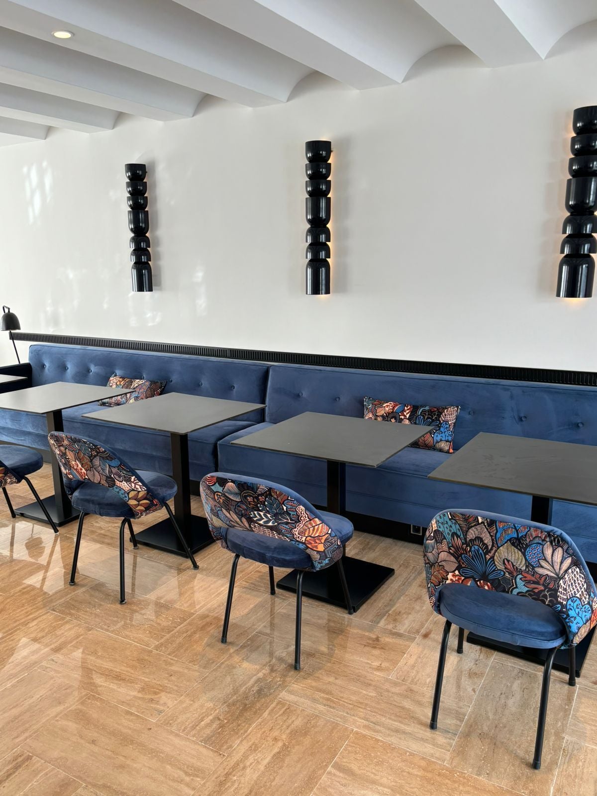 Un ristorante moderno con sedute e poltrone rivestite in blu, un muro bianco e pulito e un pavimento in legno.