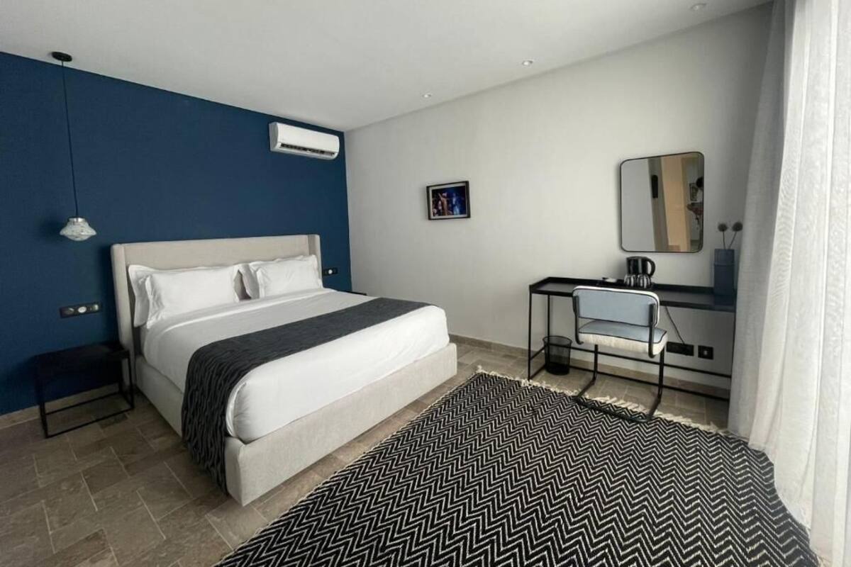 Une chambre d’hôtel moderne avec un grand lit, un bureau avec une chaise, un miroir et un petit tableau accroché au mur.