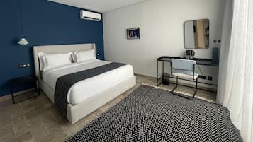 A modern hotel room with a large bed, a desk with a chair, a mirror, and a small picture on the wall.