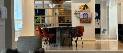 A modern living room with a grey sofa, a coffee table, and a rug. There is a kitchen area with a dining table and chairs in the background.