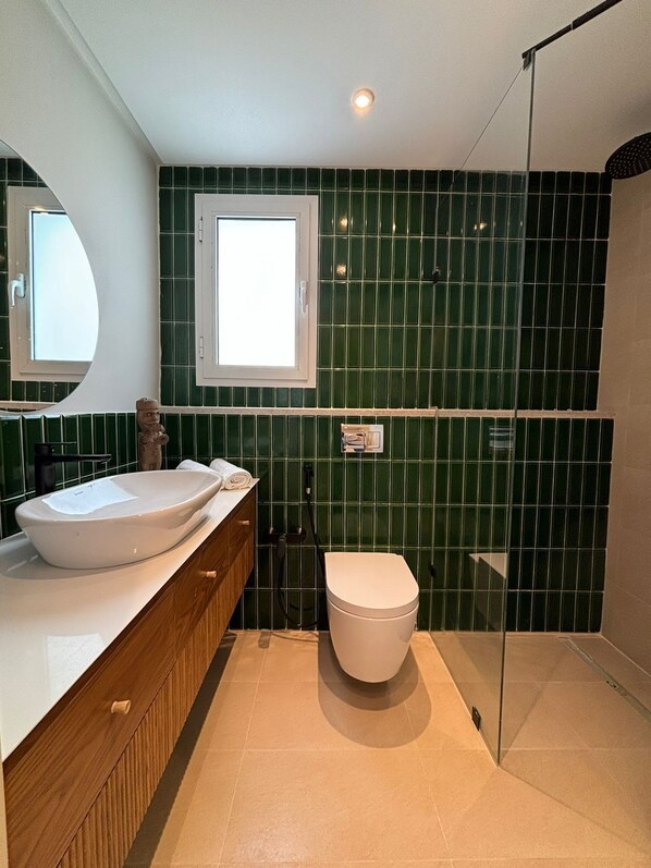 Un baño con lavamanos blanco, tocador de madera, inodoro blanco y zona de ducha.