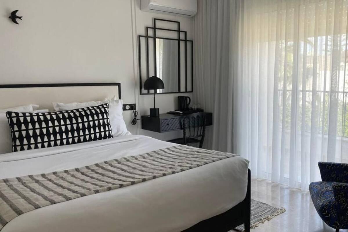 Une chambre d’hôtel avec un lit, un bureau, une chaise et une fenêtre avec des rideaux légers.