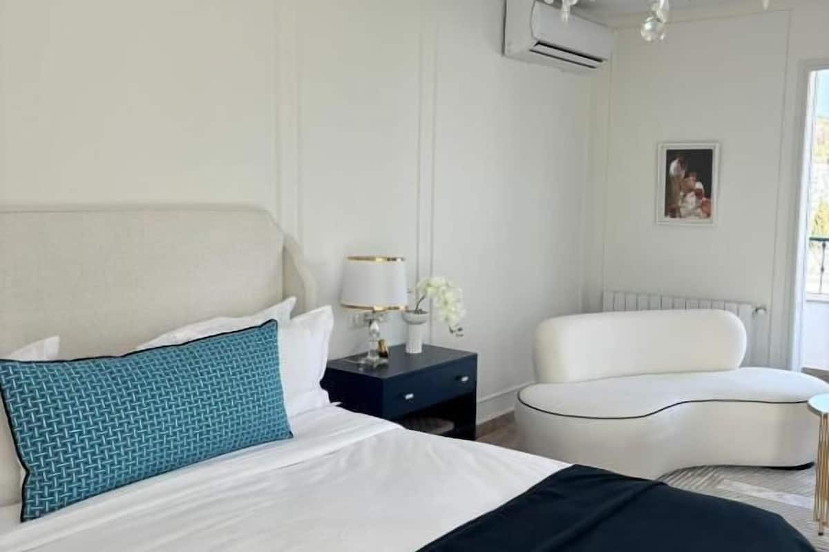 Une chambre à coucher moderne avec un grand lit, un fauteuil blanc, une petite table et un lustre.