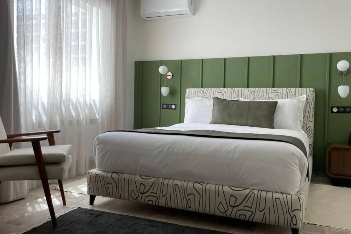 Une chambre à coucher comprenant un lit, une chaise, une table de chevet et une lampe fixée au mur.