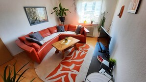 Una sala de estar moderna con un sofá seccional rojo, una mesa de centro de madera y un ventanal con vistas a edificios.