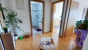 Un pasillo amplio con piso de madera, un tapete floral y plantas en macetas.
