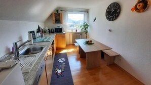 Cocina compacta con fregadero, microondas y armarios de madera. Hay una ventana que proporciona luz natural y una planta en el alféizar.