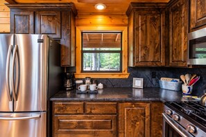 Une cuisine avec des meubles en bois, un réfrigérateur en acier inoxydable, une machine à café et une fenêtre donnant sur les arbres.