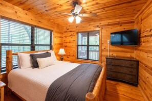 A wooden cabin bedroom with a bed, dresser, TV, and windows. - Bison Point, Smoker Grill, Corn Hole, Fire Pit, Game Table, Ladder Ball (Broken Bow)