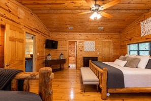 Une chambre de style rustique, avec un lit, un banc, des murs en bois, un ventilateur de plafond et une cheminée.