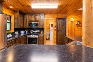 A compact kitchen with wooden cabinetry, a stainless steel refrigerator, a microwave, an oven, and a sink. - Bison Point, Smoker Grill, Corn Hole, Fire Pit, Game Table, Ladder Ball (Broken Bow)