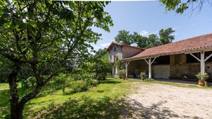 A stone building with a tiled roof, a covered porch, and a gravel driveway.
