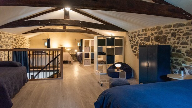A cozy attic bedroom with exposed wooden beams, a stone wall, and a built-in wardrobe.