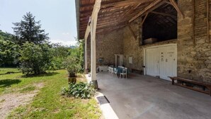 A rustic stone building with a covered patio, outdoor seating, and a stone wall.