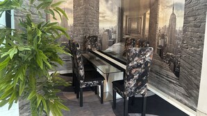 A dining area with a glass table and chairs, surrounded by a cityscape mural. - Residence Apartments Riviera Palmeraie in Abidjan (Abidjan)