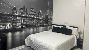 A bedroom with a bed, a nightstand, and a wall mural of a cityscape at night. - Residence Apartments Riviera Palmeraie in Abidjan (Abidjan)