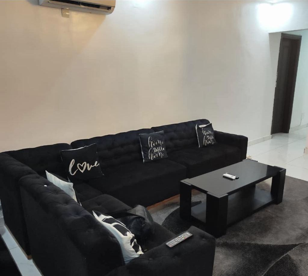 A black sofa with three pillows, a black coffee table, and a remote control on the sofa.