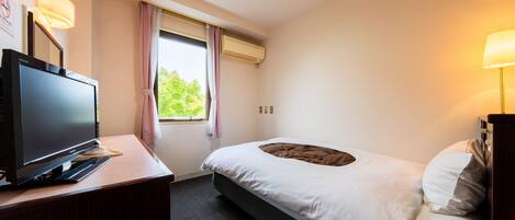 A hotel room with a bed, a desk with a television, and an air conditioning unit.