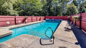 Ein Swimmingpool mit roter Umzäunung, Liegestühlen und einer Betonplattform.