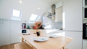 Une cuisine moderne avec une table en bois dressée pour le repas, des armoires blanches et des fenêtres de toit.