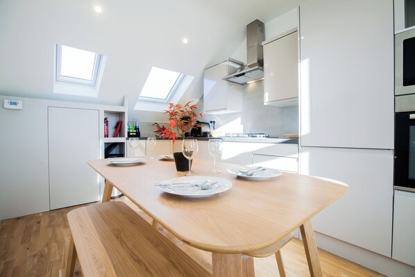 A modern kitchen with a wooden table set for dining, skylights, and white cabinetry. - Luxury Fulham 3 bedroom Garden House (London)