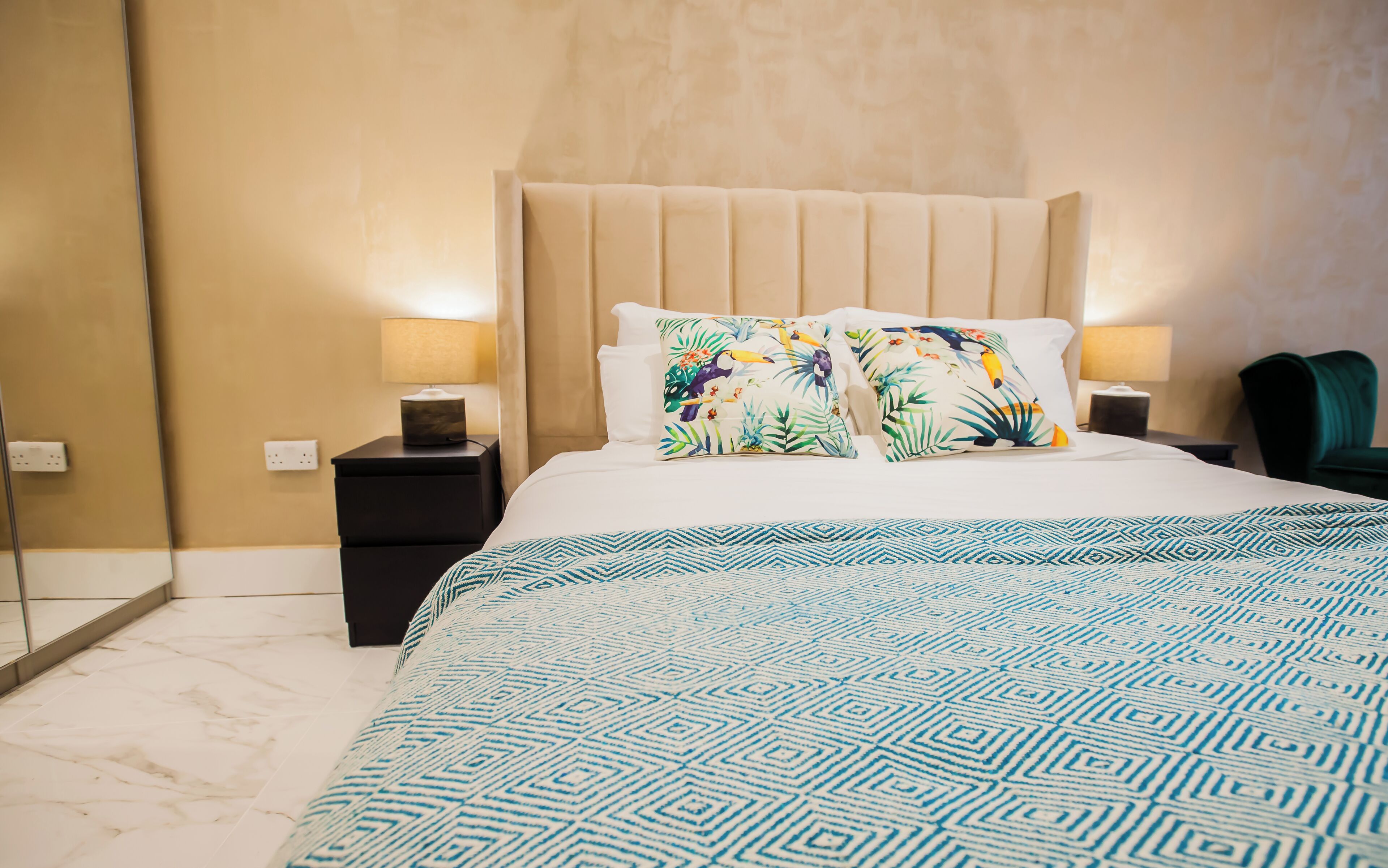 A hotel room with a large bed, two nightstands with lamps, a mirror, and a green chair.