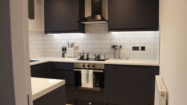 A modern kitchen with dark cabinetry, a stainless steel oven, and a white tiled backsplash. - 6guests-parking-nearstansted-accessible (Harlow)