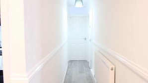 A narrow, well-lit hallway with white walls and a wooden floor, leading to a door at the end. - 6guests-parking-nearstansted-accessible (Harlow)