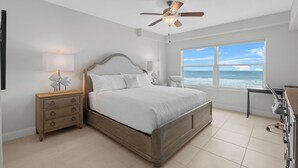 Ein Schlafzimmer mit Bett, Nachttisch, Schreibtisch, Deckenventilator und einem groĂen Fenster mit Meerblick.