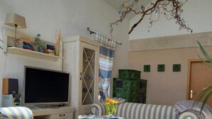 A living room with a striped sofa, a television, a cabinet, and a hanging light fixture. - Ferienhaus Bernstein in Ruhiger Lage (Kalkhorst)