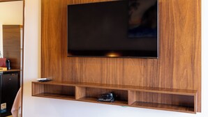 Ein modernes Wohnzimmer mit einem an einer Holzwand montierten Flachbildfernseher, einer kleinen Ablage darunter und einem zur Linken liegenden Küchenbereich.