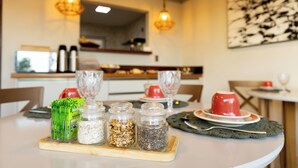 Ein Esstisch mit einer Holzbrettchen-Unterlage, darauf vier Glaskolben mit Getreide, eine rote Tasse und ein grünes Tuch.
