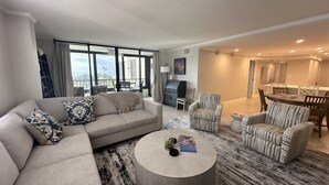 A modern living room with a sectional sofa, patterned armchairs, a round coffee table, and a dining area with a table and chairs. - Modern Condo! Beach Access, Shared Pools, and Activities! Gulf and Bay Club D409 (Siesta Key)