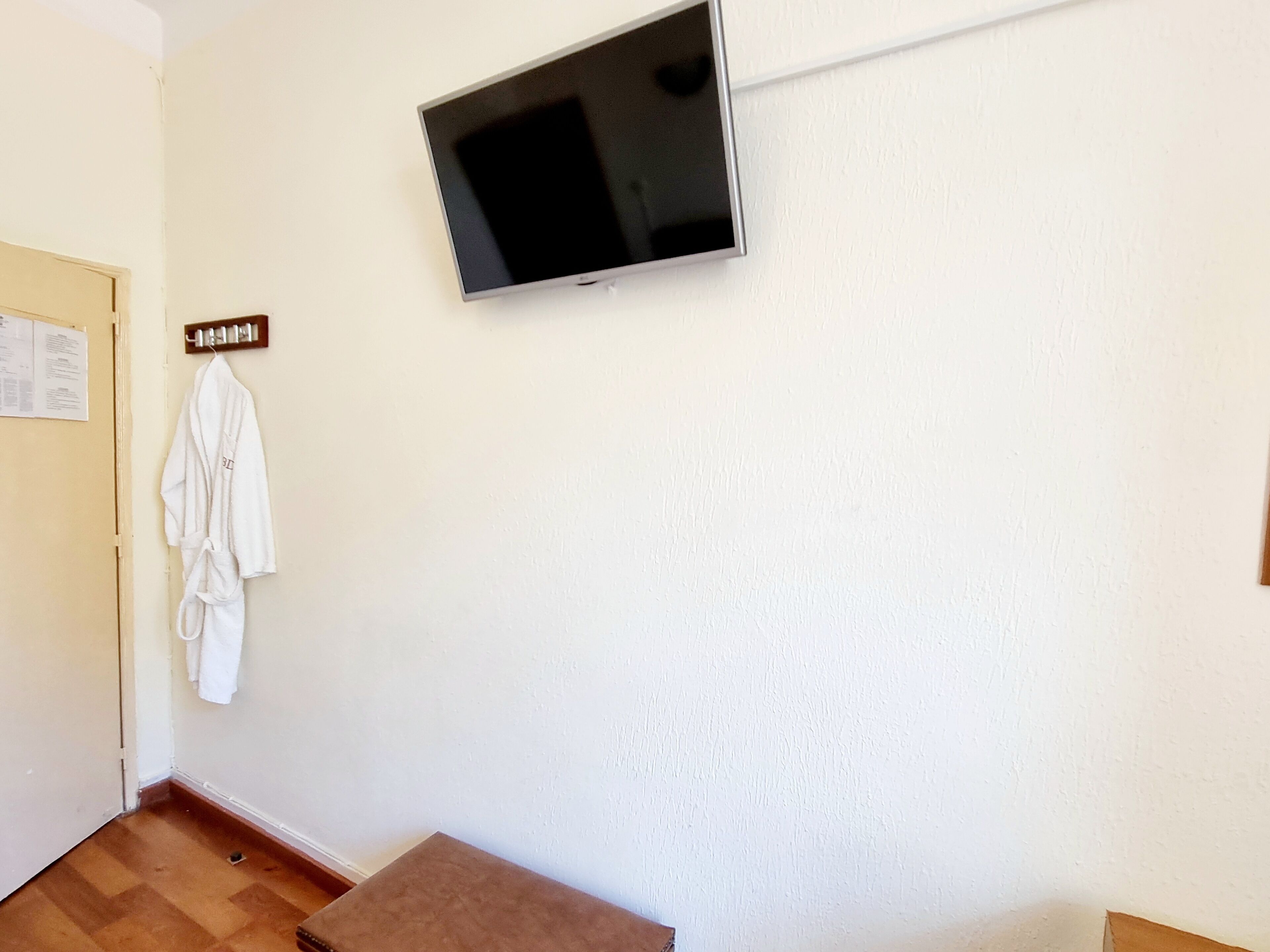A room with a flat-screen TV mounted on the wall, a wooden bench, and a white robe hanging on a hook.