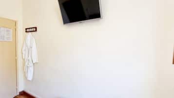 Una habitación con una televisión de pantalla plana montada en la pared, un banco de madera y una bata blanca colgada de un perchero.