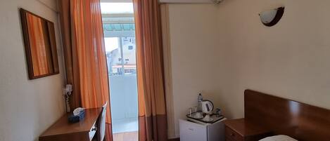A hotel room with a bed, a desk, a small refrigerator, and an air conditioning unit.