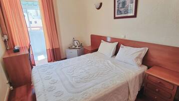 Habitación de hotel con cama, mesitas de noche, aire acondicionado instalado en la pared, un cuadro enmarcado y una ventana con cortinas.