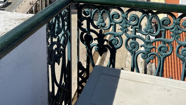 A view from a balcony with ornate black metal railings, overlooking a historic building with arched windows and a red-tiled roof. - Bons Dias (Lisbon)