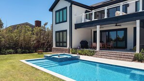 Una casa moderna de dos pisos con piscina, un patio cubierto y una chimenea de ladrillo.