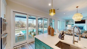 Una cocina moderna con grandes ventanales, vista a la piscina y comedor con mobiliario de exterior.