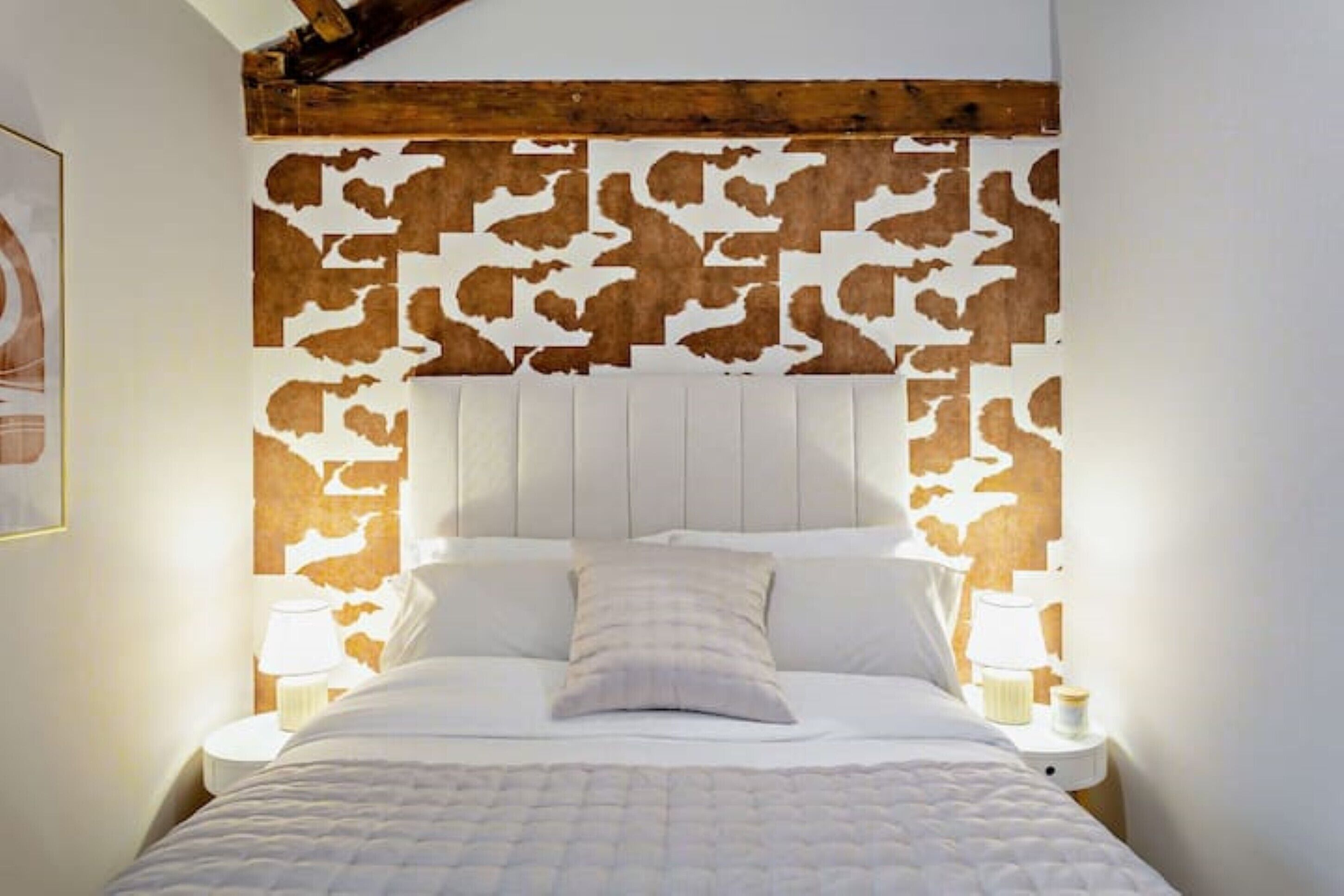 A bedroom with a bed, white headboard, and a decorative wooden headboard panel.