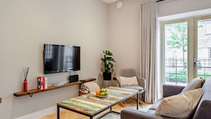 Moderni olohuone, jossa on litteänäyttöinen televisio, hedelmillä koristeltu sohvapöytä, sohva ja suuri ikkuna, jossa on verhot.