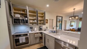 Una cocina moderna con electrodomésticos integrados, estanterías abiertas y un espejo grande sobre el lavabo.