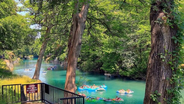 Un río con gente en balsas, rodeado de árboles y un letrero de advertencia.