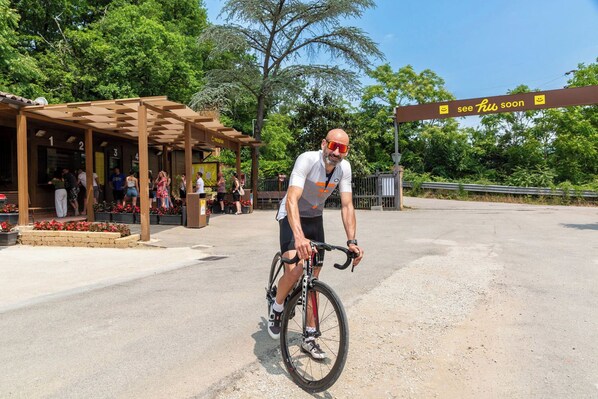 A man riding a bicycle in an outdoor area with a covered seating area and a sign that reads "see hu soon". - hu Firenze Certosa camping in town (Impruneta)