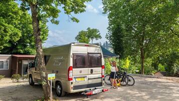A beige van parked in a campsite with trees and a small building in the background.