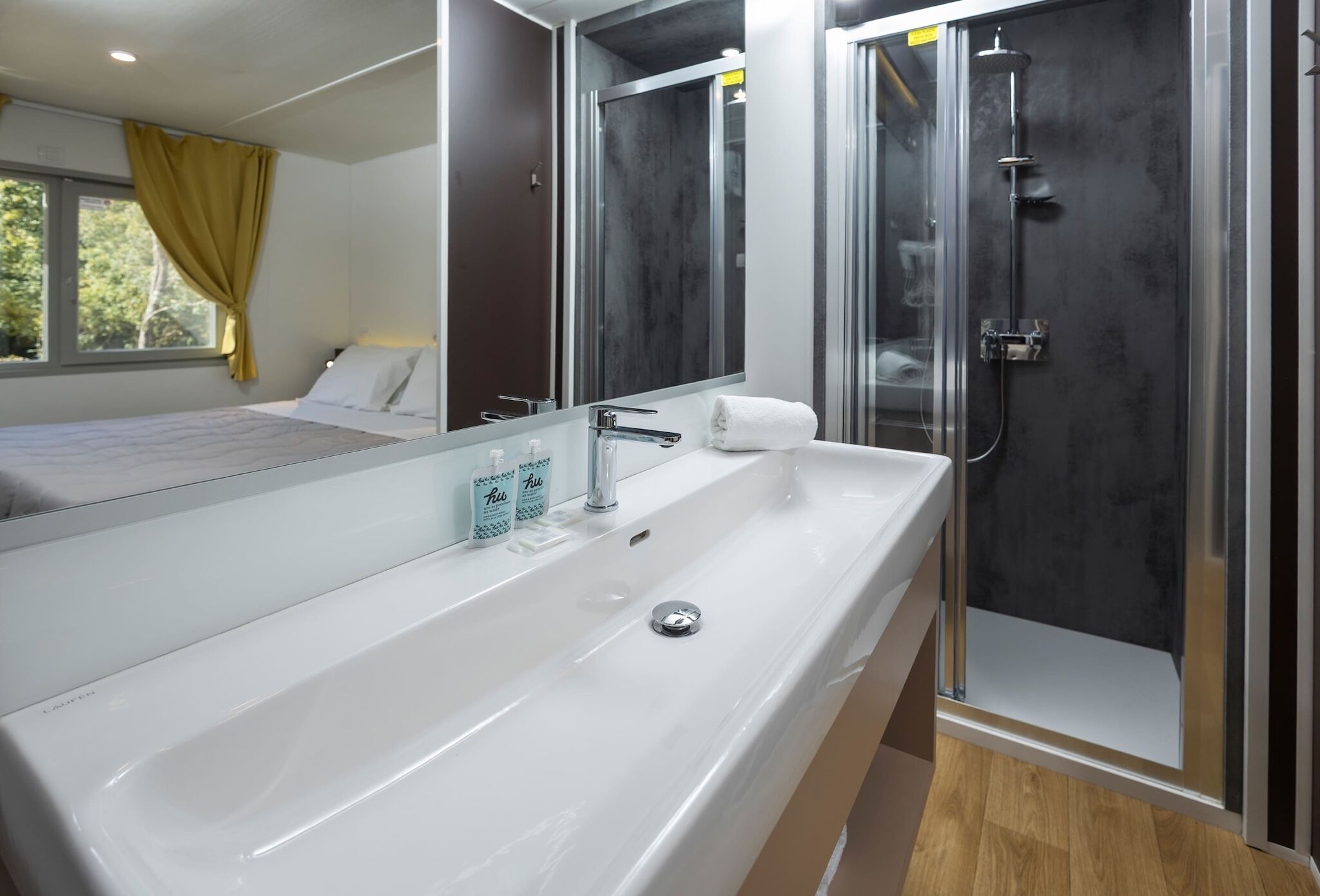 A modern bathroom with a large white sink, a mirror, and a glass-enclosed shower.
