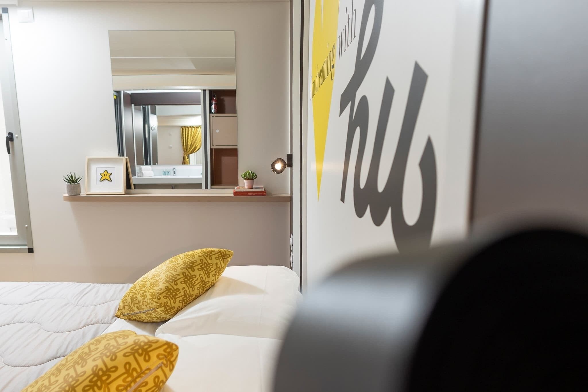 Habitación de hotel con cama, mesita de noche con lámpara, espejo y ventana.